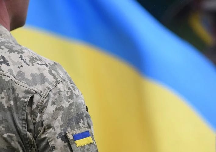 L’invasione russa dell’Ucraina rappresentata con l’immagine di un soldato ucraino in piedi davanti alla bandiera ucraina
