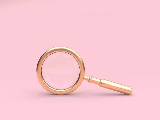  Una lente di ingrandimento dorata su sfondo rosa.