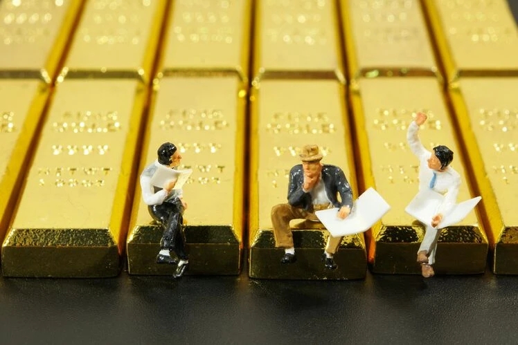 Uomini seduti su lingotti d’oro giganteschi che parlano di investimenti in oro.