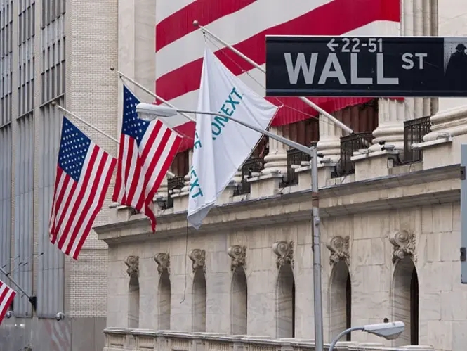Close up of a wall Street sign in New York and the stock market building in the background with US flags