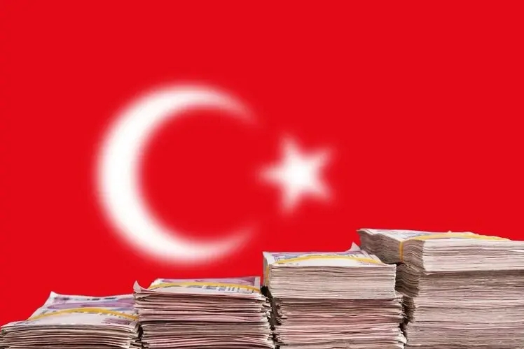 des billets de la livre turque après un effondrement historique de 15%, empilés devant le drapeau turc.