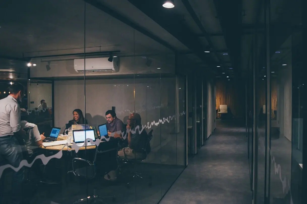 personnes travaillant et discutant dans un bureau la nuit avec des ordinateurs allumés