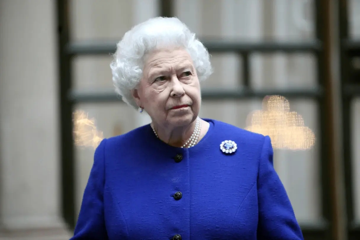 La reine Elizabeth II photographiée lors d'un événement officiel portant un costume bleu, une broche en saphir de Ceylan bleu et un collier de perles. 