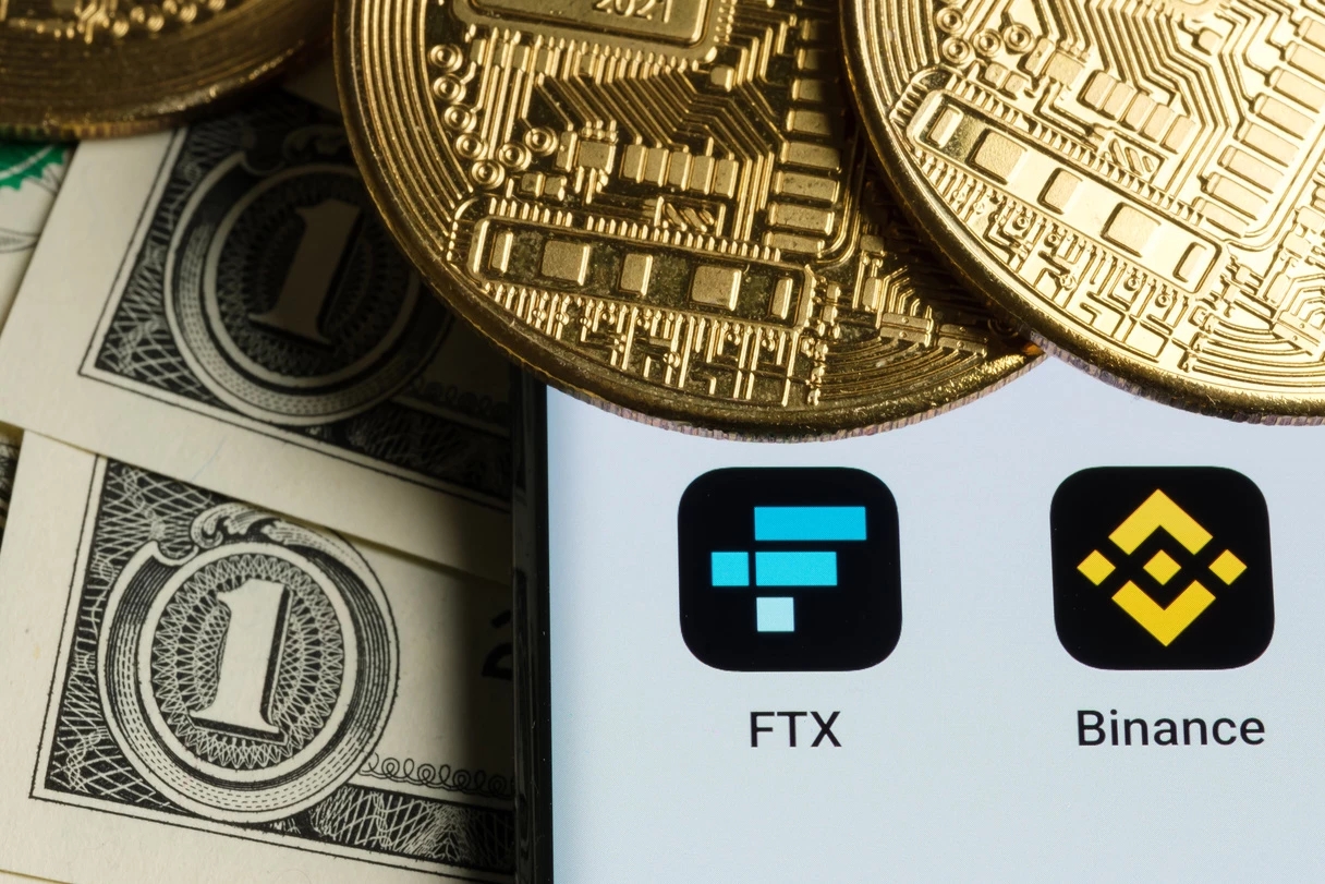 ein Bild von US-Dollarnoten, goldenen Bitcoin-Münzen und iPhone-Apps von FTX und Binance, die den gescheiterten FTX-Übernahme-Deal darstellen