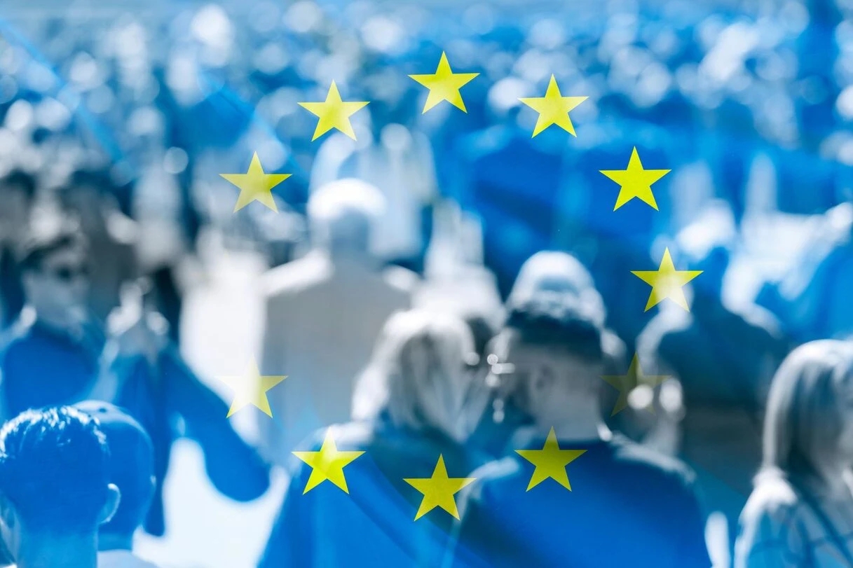Persone che camminano per la strada con la bandiera dell’UE sullo sfondo.