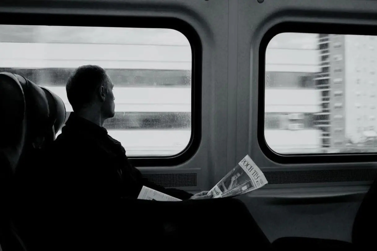 ein Schwarz-Weiß-Bild, das einen Mann mit einer Zeitung zeigt, der durch das Fenster eines Schweizer Zuges schaut, in dem Goldbarren gefunden wurden