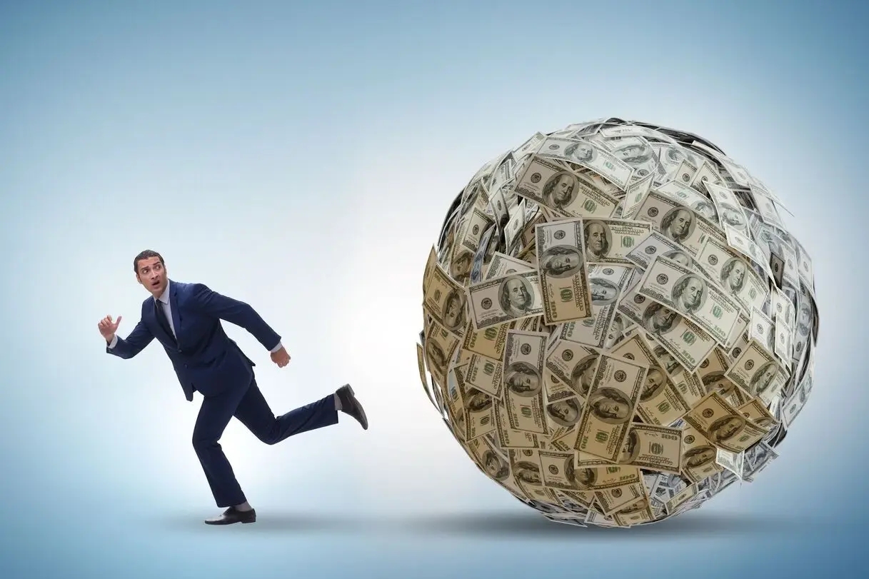a man in a suit running from a rolling paper money ball