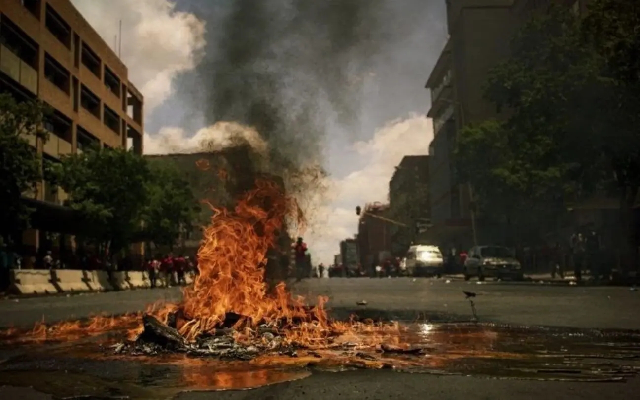 City street on fire caused by civil unrest that could intensify amid economic turmoil during which gold prices increase and investors buy gold as safe-haven asset.