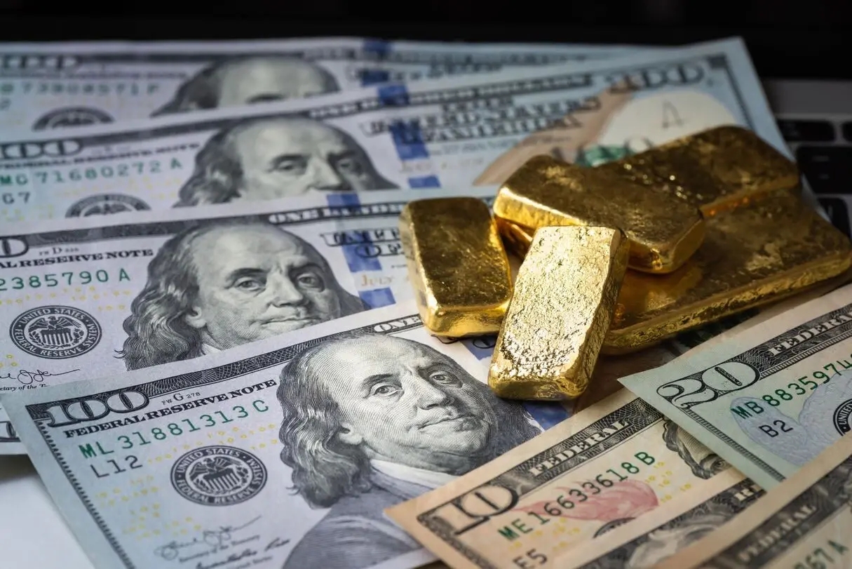 des billets de dollars avec des lingots d'or brut posés dessus symbolisant l'impression monétaire record qui est un facteur important pour le prix de l'or.