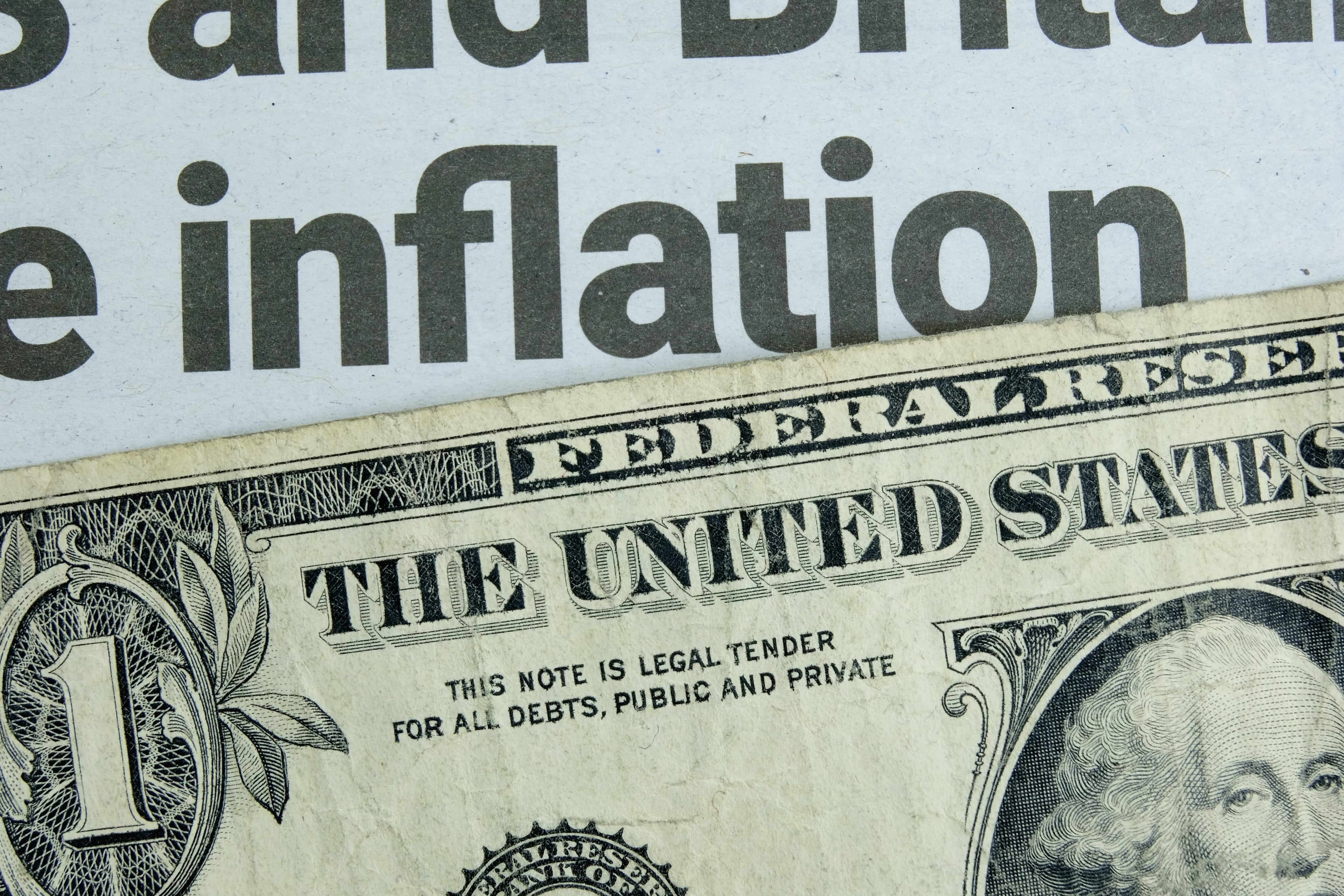 Ein 1-Dollar Schein liegt unter einer Zeitungsschlagzeile mit Nachrichten zur Inflation. Ein 1-Dollar Schein liegt unter einer Zeitungsschlagzeile mit Nachrichten zur Inflation.