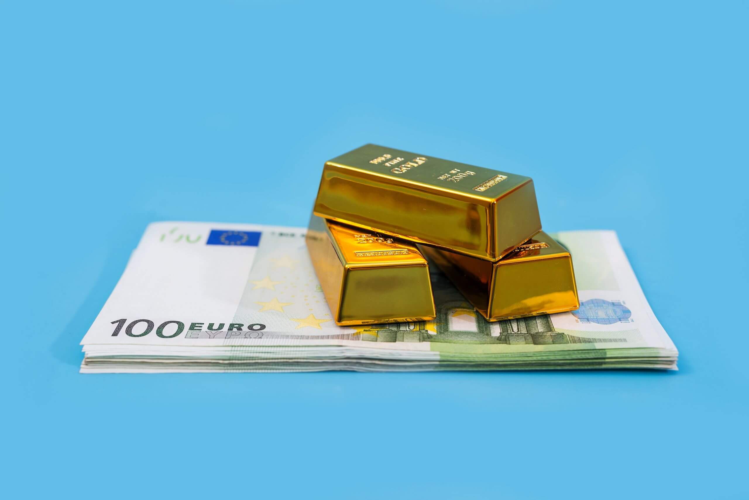 Banconote da 100 euro e tre lingotti d’oro puro su sfondo azzurro. Banconote da 100 euro e tre lingotti d’oro puro su sfondo azzurro.