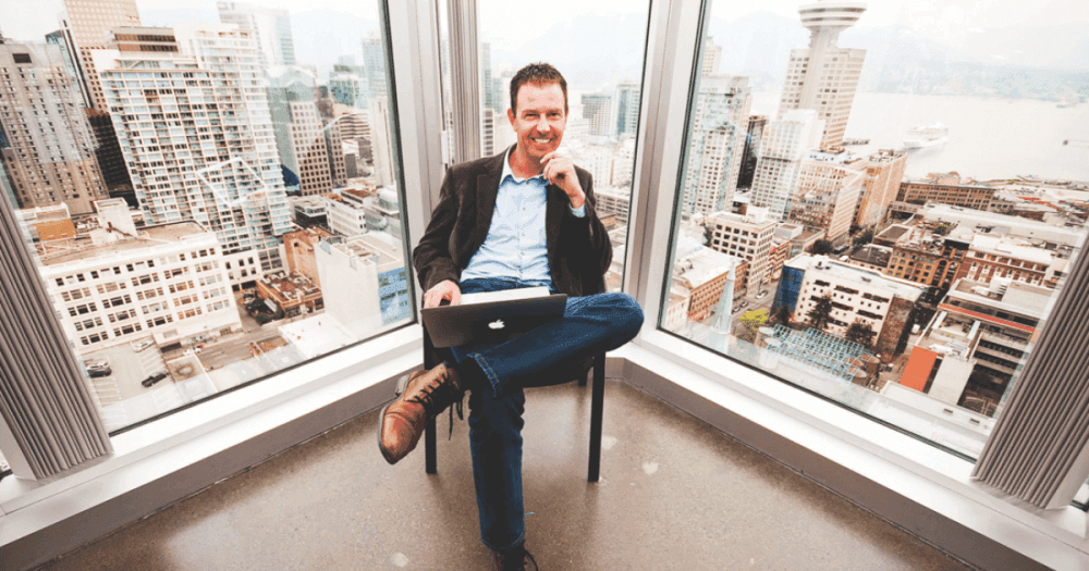 Technologie et déflation Jeff Booth, assis avec un MacBook près d'une fenêtre offrant une vue sur les gratte-ciel, publie un message sur Twitter indiquant que la technologie est la plus importante force déflationniste.