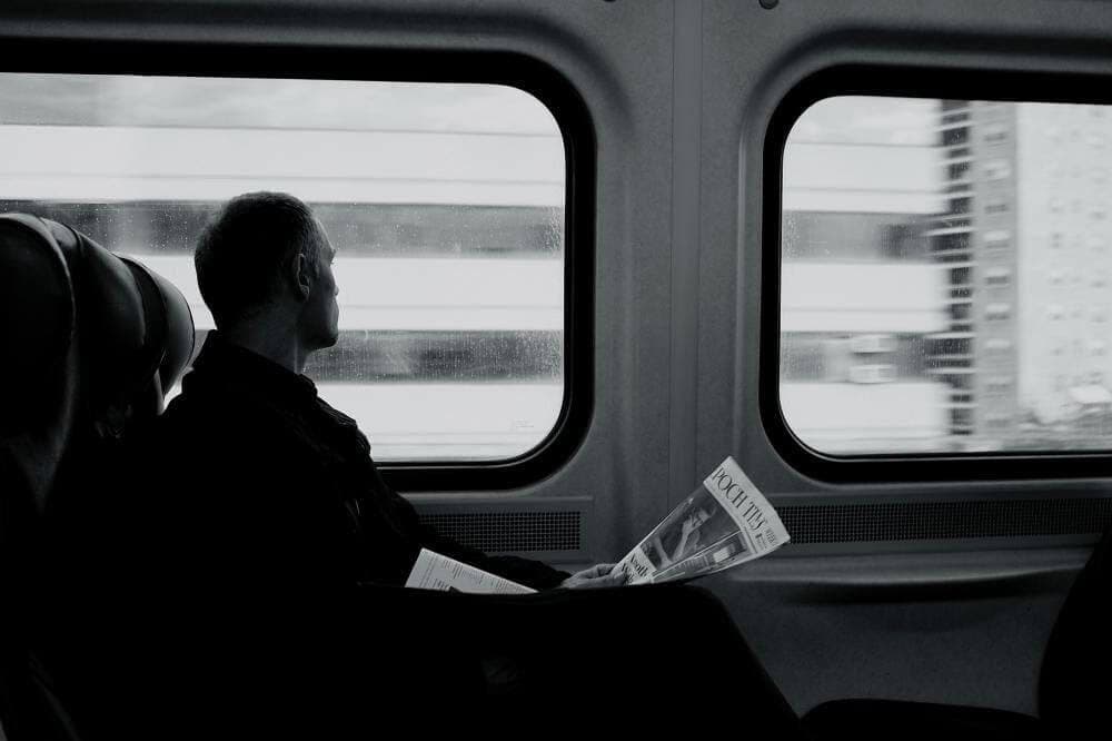 Lingotti d’oro ritrovati su un treno in Svizzera una foto in bianco e nero con un uomo con un giornale che guarda attraverso il finestrino su un treno svizzero dove sono stati trovati lingotti d'oro
